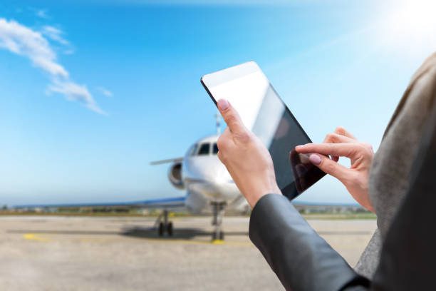 Horizontal color close-up image of woman holding digital tablet in the airport runway. Private airplane is parked at the airport asphalt runway. Beautiful blue sky with sunbeams.