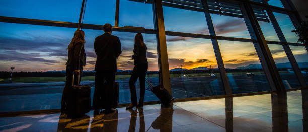 Business people looking through window at airport departure area.
